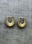A pair of small gold hoop earrings with a textured, sunburst ridged design, displayed on a textured gray linen fabric background.